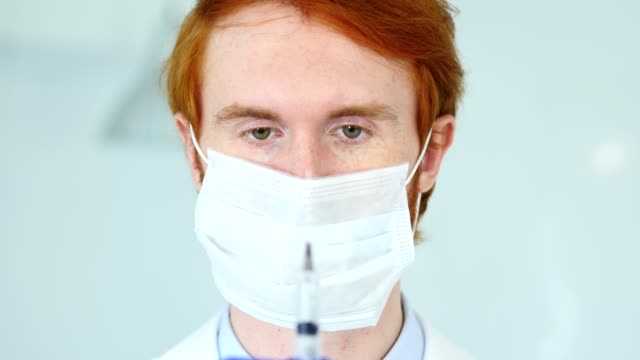 Schließen-der-rothaarige-Arzt-in-Maske-Holding-Injektion-bereit-zu-spritzen