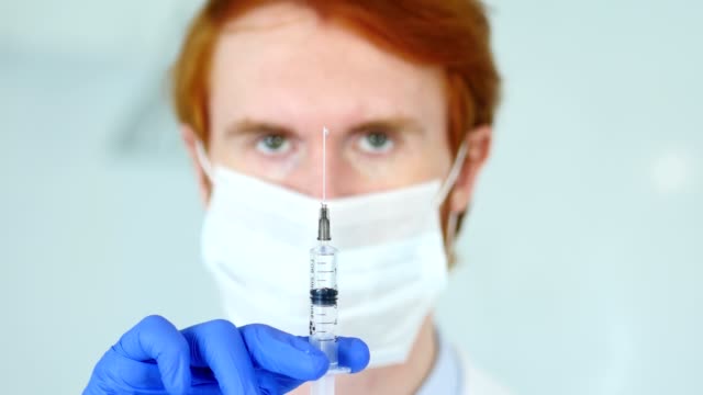 Holding-Injection,-Close-Up-of-Redhead-Doctor-in-Mask-Ready-to-inject