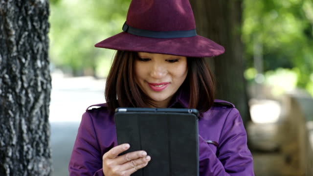 mujer-Chino-sonriente,-vestida-de-púrpura-utilizando-el-tablet-en-el-parque,-retrato