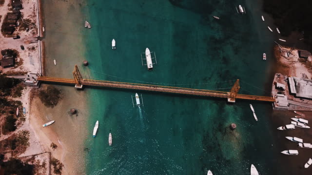 Barcos-que-pasan-bajo-el-puente-amarillo-de-Nusa-Ceningan-en-Bali-con-cristal-claro-de-agua-4K