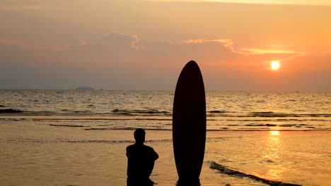 4-K.-Silhouette-der-Surfer-Mann-sitzt-am-Meeresstrand-mit-langen-Surfbretter-bei-Sonnenuntergang-am-tropischen-Strand