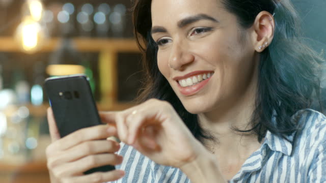 Close-up-Portrait-Shot-of-a-Beautiful-Young-Woman-Smiling-and-Using-Mobile-Phone.-In-the-Background-Stylish-Cafe.