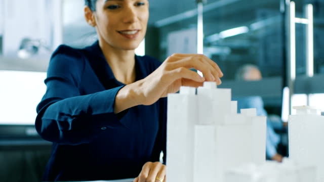 Female-Architectural-Designer-Adds-Component-to-a-Building-Model,-She-Works-on-a-City-District-Urban-Planning-Project.-Beautiful-Woman-in-Stylish-Office.