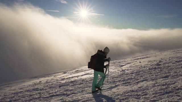 Stabilized-flow-motion-shot-of-girl-hiking-on-snow-in-Slovak-mountains-above-clouds-during-sunset-in-winter