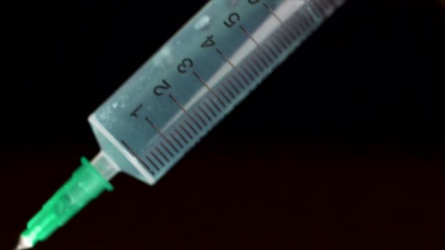 Hand-holding-a-syringe,-the-syringe-is-filled-with-clear-liquid-is-isolated-on-black-background.-Hypodermic-syringe-that-is-being-filled-with-vaccine