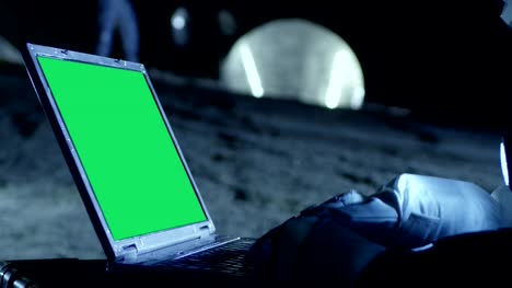Astronaut-auf-dem-fremden-Planeten-arbeitet-auf-einem-Mock-up-Green-Screen-Laptop.-Im-Hintergrund-ihrer-Crew-Mitglied-und-lebendige-Station.-Kolonisation-Konzept.