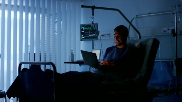 In-the-Hospital,-Recovering-Male-Patient-Uses-Laptop-while-Lying-on-the-Bed.-Using-Technology-to-Communicate-with-Loved-Ones.