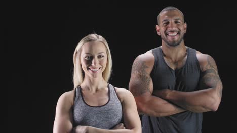 Portrait-shot-of-an-athletic-man-and-woman-with-their-arms-crossed,-and-smiling-on-a-dark-background