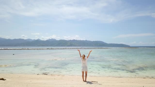 TOMA-AÉREA.-Mujer-de-pie-de-la-impresionante-playa-en-brazos-de-Bali-abiertos.-Drone-volando-por-encima-de-la-impresionante-playa-de