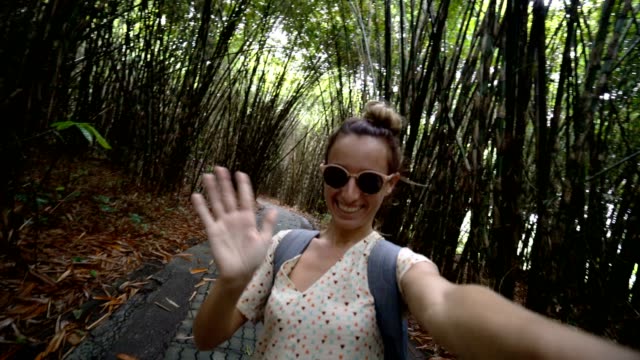 Young-woman-takes-a-selfie-portrait-in-bamboo-forest-located-in-Bali,-Indonesia.-People-travel-fun-technology-sharing-social-media-concept.-4K