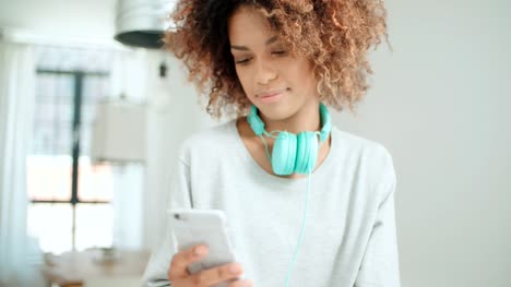 Schöne-junge-Afro-Amerikanerin-SMS-auf-dem-Handy-zu-Hause.