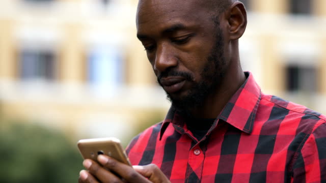 attraktive-schwarze-Afrikaner-Tippen-auf-seinem-Smartphone-auf-der-Straße