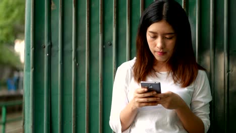Junge-Asiatin-mit-Smartphone-Senden-von-SMS-Nachrichten-im-öffentlichen-Park.