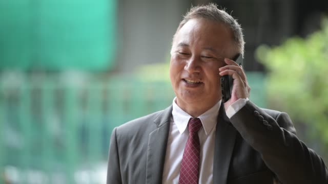 Reife-japanischer-Geschäftsmann-mit-Telefon-in-den-Straßen-im-freien