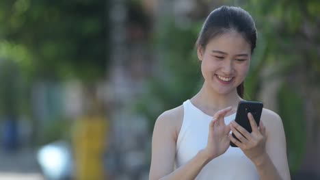 Joven-empresaria-asiática-hermosa-feliz-con-teléfono-al-aire-libre