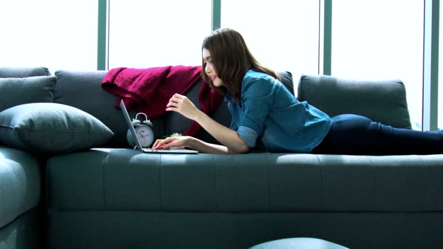 attraktive-asiatische-Frau-genießen-erholsame-Zeit-mit-Laptop-im-Wohnzimmer-zuhause-Hintergrund