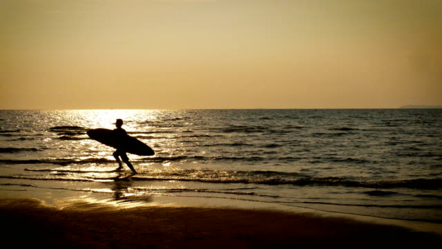 Silueta-de-4-K.-de-surf-feliz-joven-hombre-corriendo-con-tablas-de-surf-largo-al-atardecer-en-playa-tropical.-surfista-en-la-playa-en-la-orilla-del-mar-en-el-atardecer-con-la-hermosa-luz-del-sol-reflejan-en-la-superficie-del-agua.