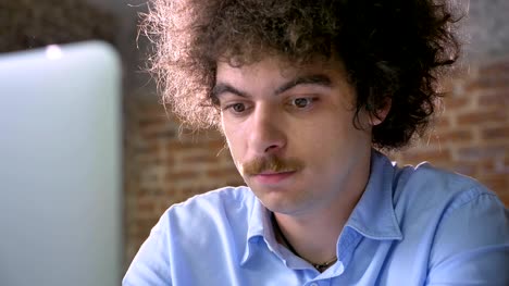Nerdy-young-programmer-with-mustache-and-curly-hair-typing-working-on-laptop,-serious-and-concentrated