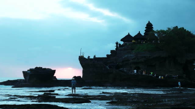 ein-Mann-sieht-den-Sonnenuntergang-in-Tanah-Lot-auf-Bali-bei-Ebbe