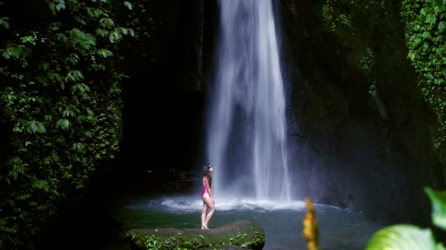 Frau-im-Badeanzug-entspannend-am-Wasserfall-in-Bali,-Indonesien.-Tropischer-Wald-und-Wasserfall