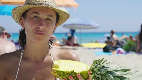 Porträt-eines-schönen-jungen-Mädchens-am-Meer,-eine-Ananas-in-einem-Badeanzug-in-einem-Strohhut-Strand-Hintergrund-halten.