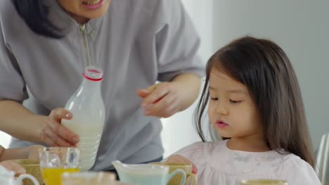 Asiatische-Mutter-gießt-Milch-für-Kinder-während-des-Frühstücks