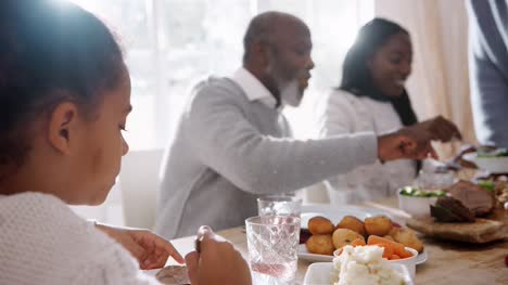 Multi-generation-mixed-race-family-sitting-at-the-table-serving-each-other-Sunday-dinner-at-home,-close-up,-backlit