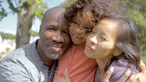 Afro-americana-rizada-hija-abrazando-a-los-padres-felices-en-el-Parque