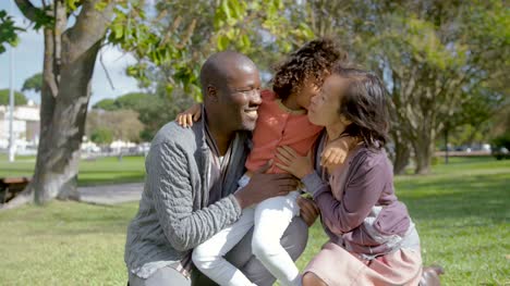 Mixed-race-daughter-hugging-and-kissing-parents-in-park