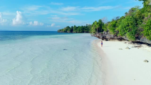 Aerial:-woman-walking-on-tropical-beach,-scenic-turquoise-water-and-white-sand,-Tomia-Island,-Wakatobi-marine-national-park,-Indonesia,-paradise-travel-destination
