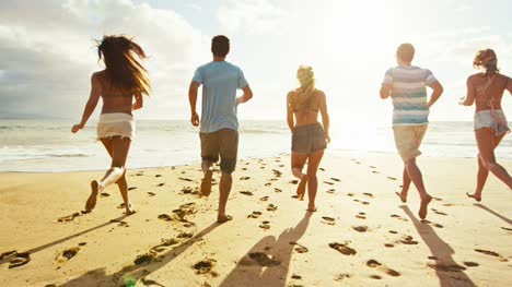 Grupo-de-amigos-que-se-divierten-caminando-por-la-playa-al-atardecer