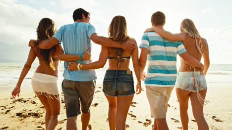 Group-of-friends-having-fun-walking-down-the-beach-at-sunset