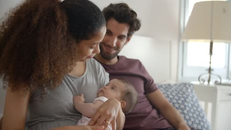 Parents-Cuddling-Baby-Daughter-In-Bedroom-At-Home
