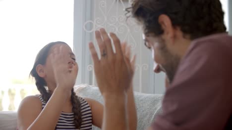 Father-And-Daughter-Playing-Clapping-Game-Sitting-On-Sofa