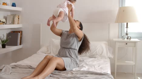 Mother-Playing-With-Baby-Daughter-In-Bedroom-At-Home