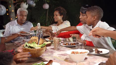 Familia-de-generación-negro-multi-que-sirven-comida-en-la-mesa-al-aire-libre