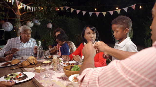 Multi-generation-black-family-eating-food-at-table-outdoors