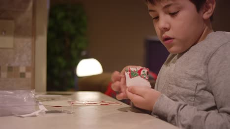 Ein-Junge-sitzt-an-der-Küchentheke-und-legt-einen-Weihnachtsaufkleber-auf-ein-Blatt-Papier
