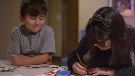 Un-niño-mirando-a-su-hermana-mientras-dibuja-y-mira-a-través-de-su-teléfono-en-busca-de-inspiración