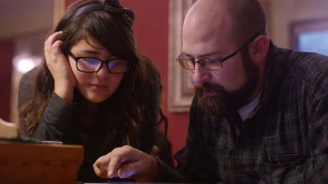 Un-padre-y-una-hija-en-la-mesa-mirando-una-tableta-juntos