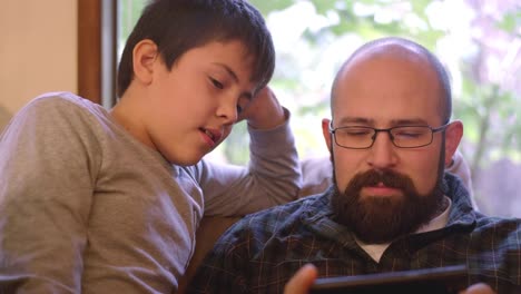 Vater-und-Sohn-sitzen-und-sprechen-auf-einer-Couch-zu-Hause,-während-der-Vater-sein-Handy-benutzt
