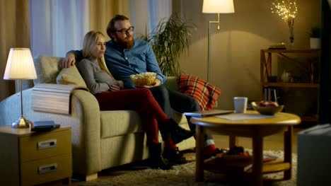 Im-Abend-sitzen-Mann-und-Frau-auf-dem-Sofa-Watching-TV-und-fressen-Popcorn.-Das-Wohnzimmer-ist-Cozy.
