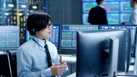 In-the-Network-Operations-Center-Trader-Makes-Personal-Client-Call-with-a-Headset.-In-the-Background-Traders-Discuss-Data-Shown-on-Monitors.