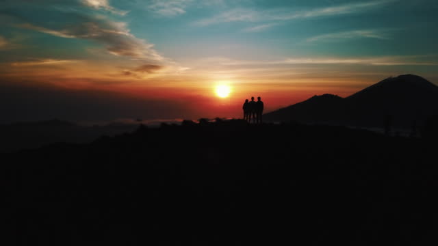 People-Standing-On-Top-Of-Active-Volcano-Mount-Batur-In-Bali-At-Sunrise-With-Clouds-Reveal-Aerial-Shot-4K