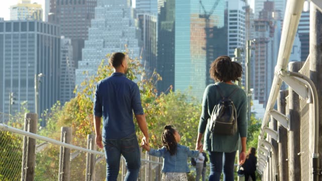 Couple-with-young-daughter-walking-on-footbridge,-back-view