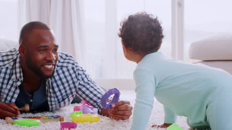 Padre-negro-joven-acostado-en-el-piso-jugando-con-su-hijo