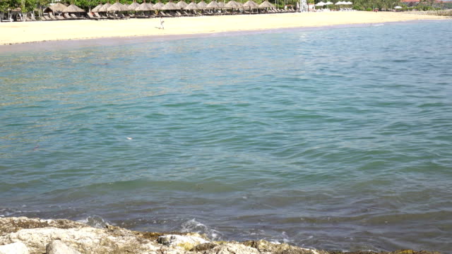 Wellen-des-warmen-Meeres-laufen-am-Sandstrand-des-tropischen-Resorts-mit-Sonnenschirmen-und-Liegestühlen