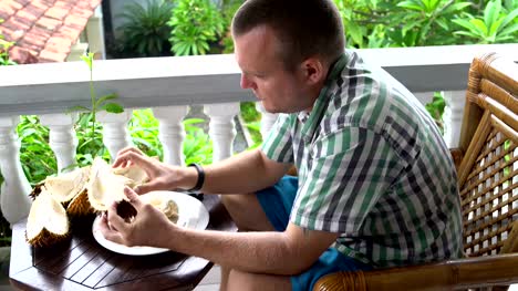 Un-hombre-sentado-en-un-balcón-limpia-durian-con-sus-manos