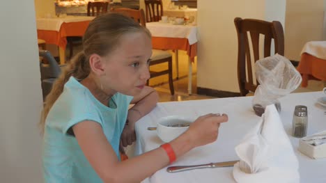 Adorable-girl-eating-porridge-from-bowl-for-breakfast-in-cafe