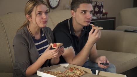 Atractiva-pareja-joven-sentada-en-el-sofá-y-comer-pizza